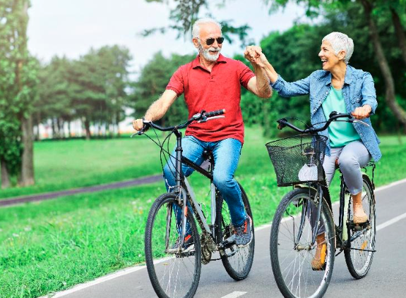 Senior couple riding their bikes in a park while holding hands and smiling