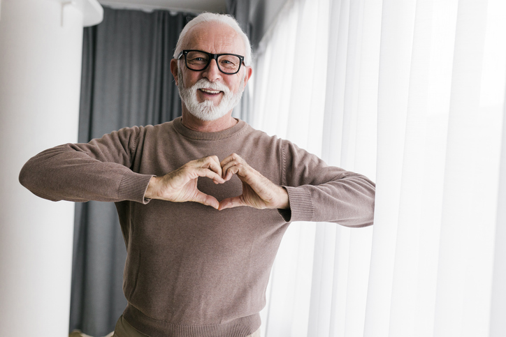Portrait of a senior man at home showing a heart-shaped symbol