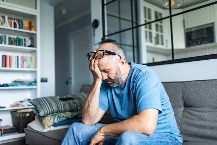 Middle aged man holding his head sitting in his living room