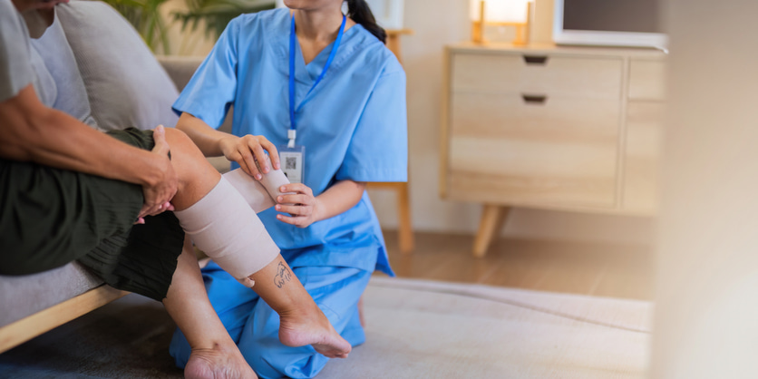 nurse helping patient wrap leg in compression bandage
